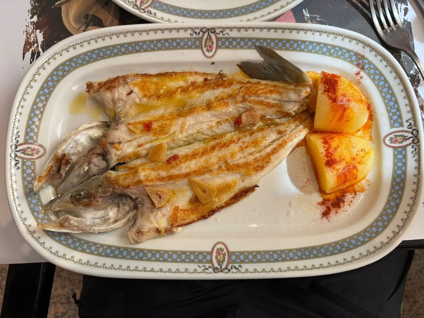 Pescado abierto a la plancha con ajos y patatas, en fuente ovalada con orla azul