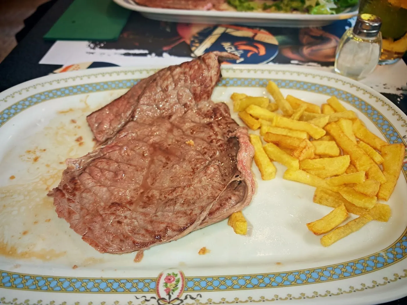 Filete de ternera a la plancha con patatas fritas, en fuente ovalada con orla azul